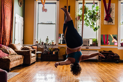 a plus size white woman with blond hair hangs upside down on silks in an aerial yoga class