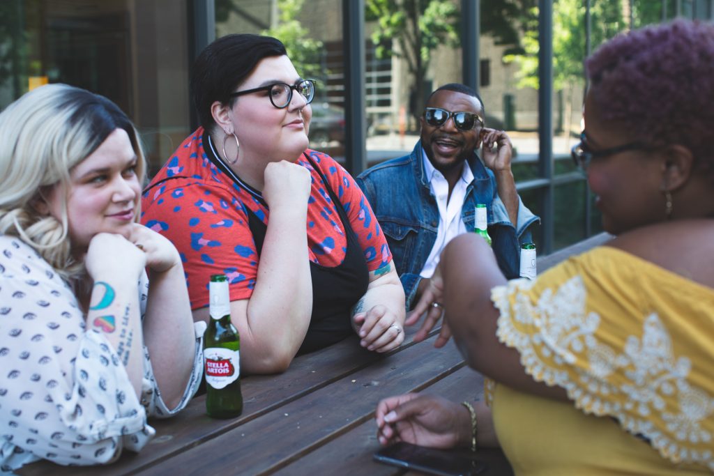 Four people of different sizes, genders, and races chat on a patio.