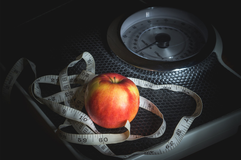 An apple and a body tape measure sit on top of a scale