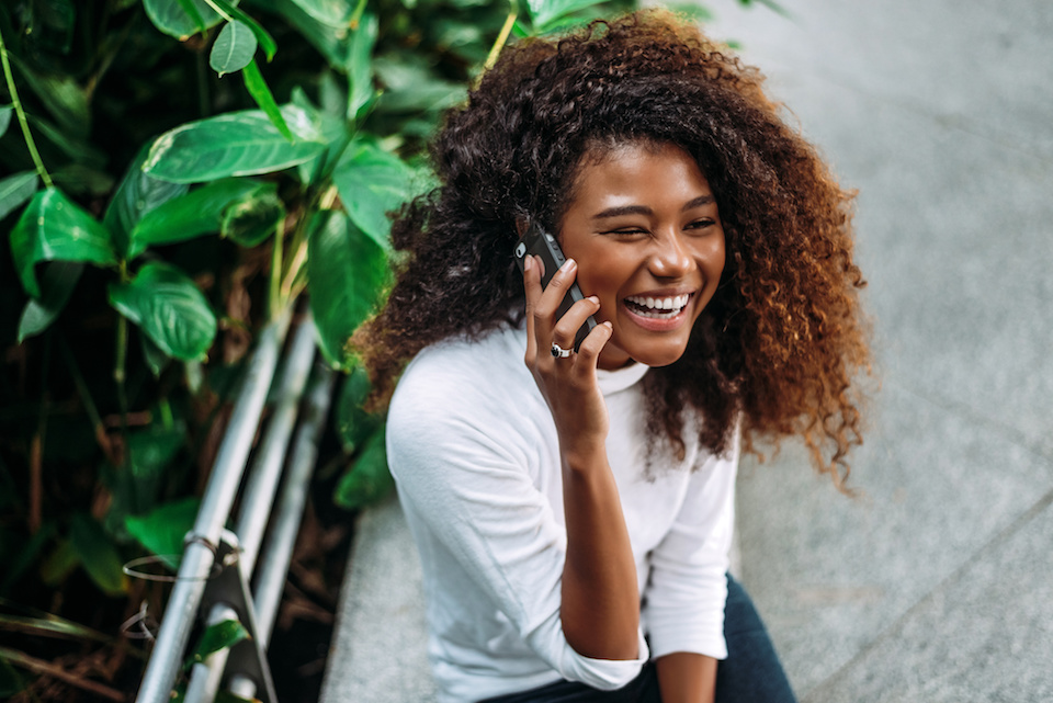 Portrait of smiling curly haired Black woman talking on the phone.
