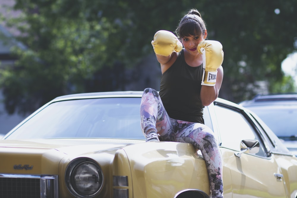 a woman with brown hair and boxing gloves sits on top of a yellow car